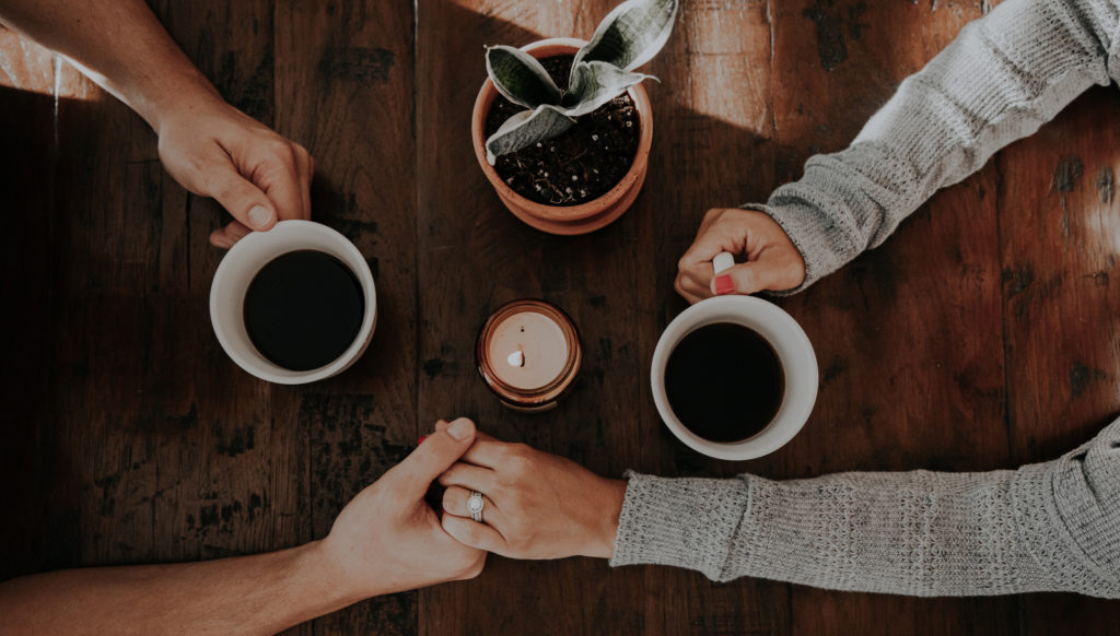table top with couple holding hands drinking coffee
